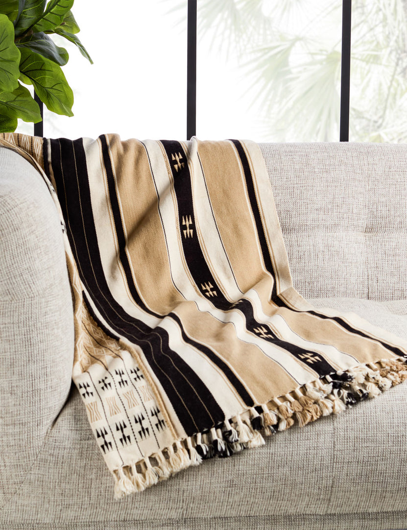 | The Sita throw blanket lays on a natural-toned linen sofa in a room with floor to ceiling windows and house plants