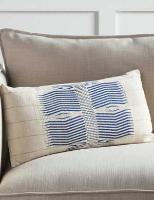 The Imli ivory and blue throw pillow sits on a gray linen sofa in a room with accented white walls
