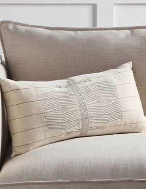 The Imli ivory and gray throw pillow sits on a gray linen sofa in a room with accented white walls