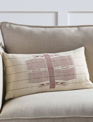 The Imli ivory and red throw pillow sits on a gray linen sofa in a room with accented white walls