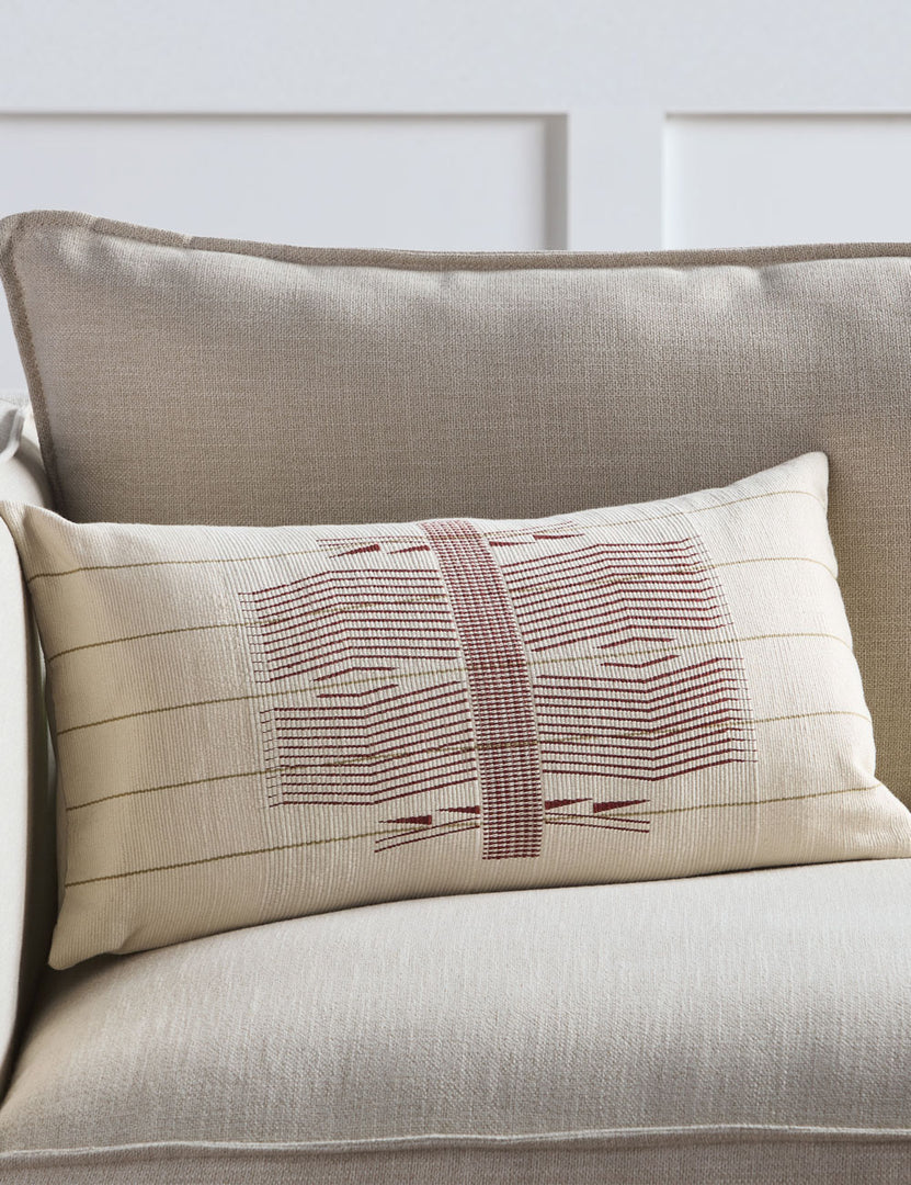 #color::red #fill::down #fill::polyester | The Imli ivory and red throw pillow sits on a gray linen sofa in a room with accented white walls