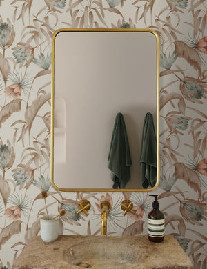 Natural-toned Tropical Wallpaper by Rylee + Cru is in a bathroom with a rounded gold mirror and a stone sink with gold hardware