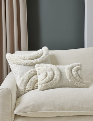 The arches ivory pillow in both sizes are in a studio room sitting atop a natural linen sofa