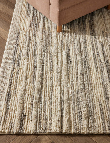 #color::gray #size::2--x-3- #size::2-6--x-8- #size::5--x-7-6- #size::8--x-10- #size::9--x-12- #size::10--x-14- | The Rizzoli gray rug sits on a chevron wooden floor under a natural accent chair