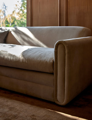 The Eleanor oatmeal beige sofa sits atop a brown rug in a room with accented wooden walls and a large window