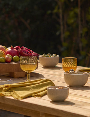 The Set of 4 mustard yellow Essential Cotton Dinner Napkins by Hawkins New York sits atop a wooden dining table in an outdoor space with yellow tinted glasses and white bowls