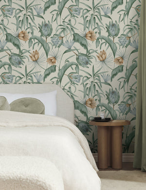 Green-toned Tropical Wallpaper by Rylee + Cru is in a bedroom with a wooden nightstand, linen framed bed, and olive linens