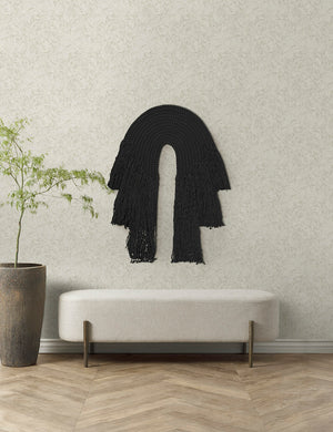 The black forte wall hanging hangs on an ivory wall above a white linen bench