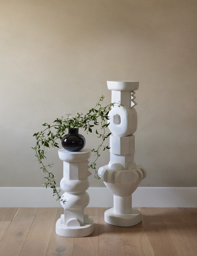 #size::tall #size::short | The Toivo short and tall pedestals stand next to each other in a room with a black glossy vase and neutral-toned walls