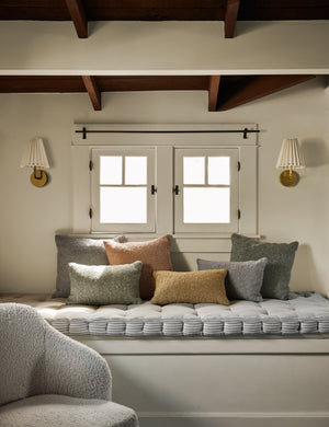 Manon linen boucle pillows sit on a gray linen cushioned bench in a room with two golden cosette sconces and wooden beamed ceilings