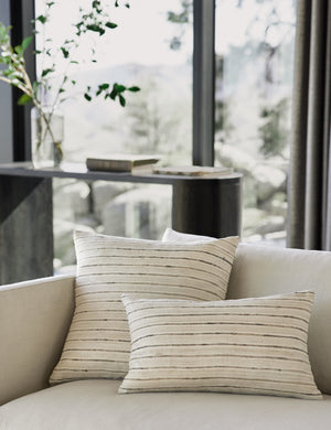 Marit neutral silk pillow with striated lines sits on a natural linen couch in a living room with a black console table in the background