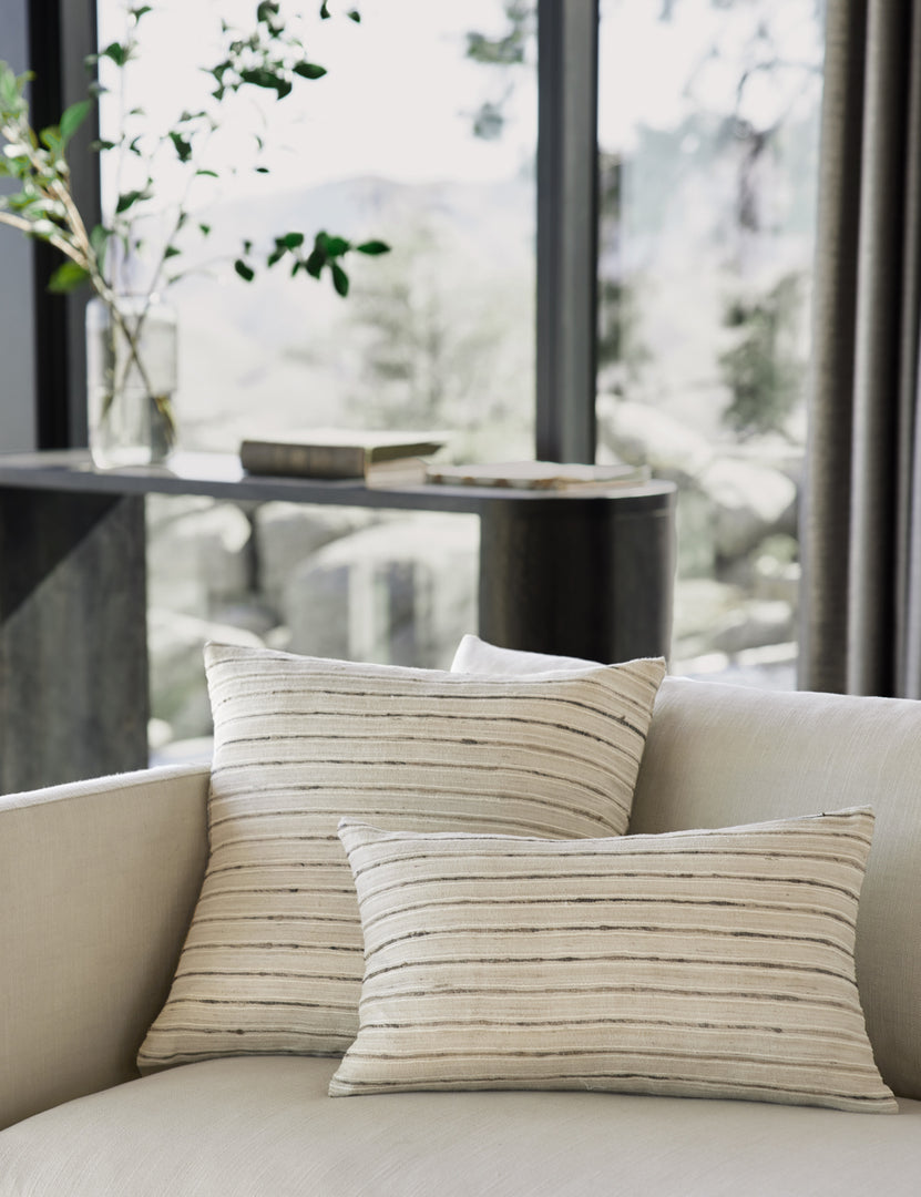 #size::12--x-20- #size::20--x-20- | Marit neutral silk pillow with striated lines sits on a natural linen couch in a living room with a black console table in the background