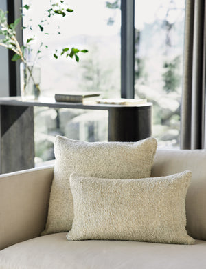 The manon linen oatmeal cream boucle pillow in both sizes lay on a white linen sofa in a living room with a black wooden sideboard