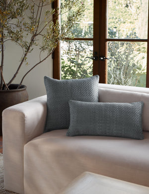 The victor dusty blue pillow in both sizes sit together on a natural linen sofa in front of a black-framed window