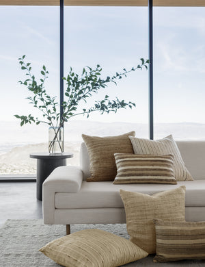 The Danique earth-toned striped silk lumbar throw pillow sits on an ivory sofa in a room with floor to ceiling windows