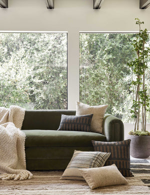 The Kellan square and lumbar throw pillows sit on a green velvet sofa on a textured natural carpet