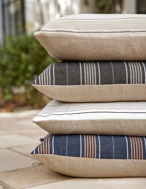 The Whitehaven indoor and outdoor square pillow is stacked with the other colorways in an outdoor space