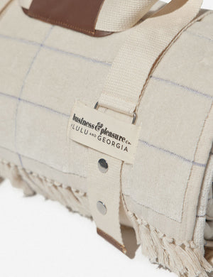 Close-up of the cream popcheck cotton beach blanket by business and pleasure co wrapped up in the leather-handled strap
