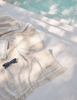 Pop check Beach Towel by Business & Pleasure Co sits by a pool with sunglasses and a book atop it