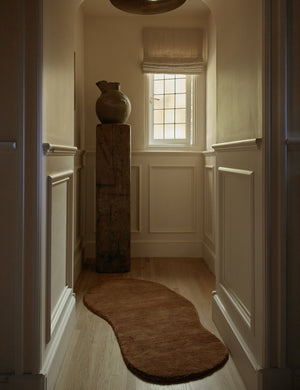 The shorter Rangely Rug lays in a hallway with high ceilings, a tall wooden sculptural object, and a narrow window