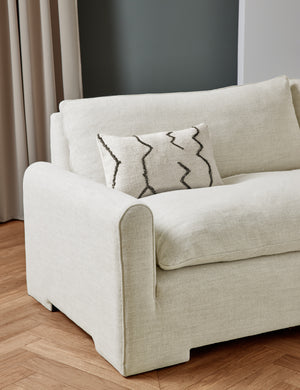 The Rupert natural linen sofa sits in a studio room with an ivory flatweave pillow with black accents sitting atop it