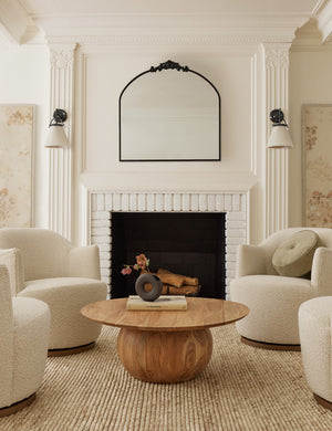 Four natural boucle margie swivel chairs sit around a wooden circular coffee table atop a sand Kenzi rug.
