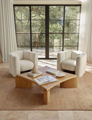 The Heritage wheat rug lays in a living space with floor to ceiling french doors and two boucle accent chairs