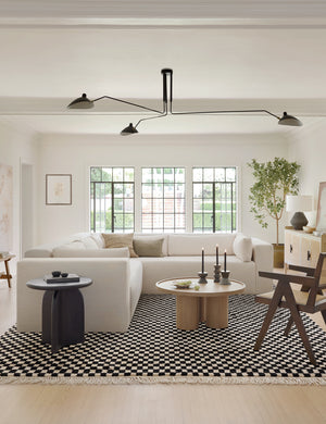 Black and white Checkerboard Rug by Sarah Sherman Samuel lays in a living room with a cream sectional and a round wooden coffee table