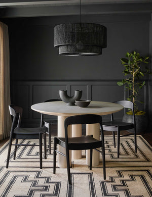 Mojave Round Dining Table sits in a room with black accented walls, black dining chairs, and a black and neutral patterned rug