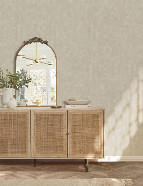 | The tulca vanity brass mirror sits against a wall on a rattan sideboard next to a white vase