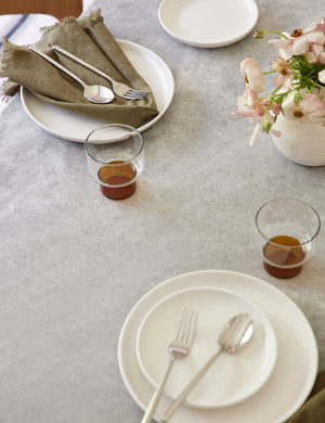 The Set of 4 olive green Essential Cotton Dinner Napkins by Hawkins New York sits on a stone dining table in a dining room with white dinnerware and amber tinted glasses
