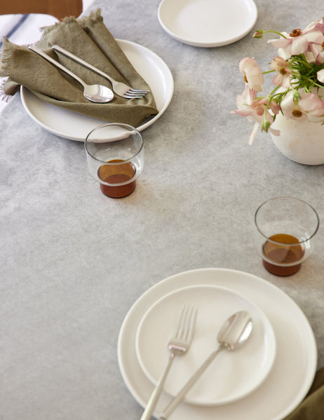 #color::olive | The Set of 4 olive green Essential Cotton Dinner Napkins by Hawkins New York sits on a stone dining table in a dining room with white dinnerware and amber tinted glasses