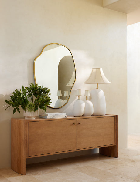 #size::large | The large puddle mirror hangs on a cream wall over a wooden sideboard that has three sculptural lamps atop it