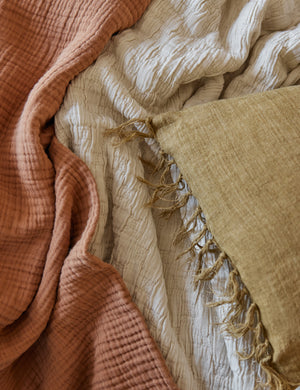 The Ojaj greige cotton matelassé coverlet by pom pom at home lays with a terracotta throw blanket and a mustard tassel pillow