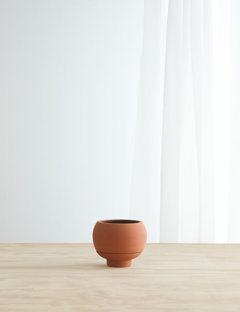 #color::terracotta | Sutton Ceramic Self-Watering Planter by Greenery Unlimited in terracotta sits on a wooden table