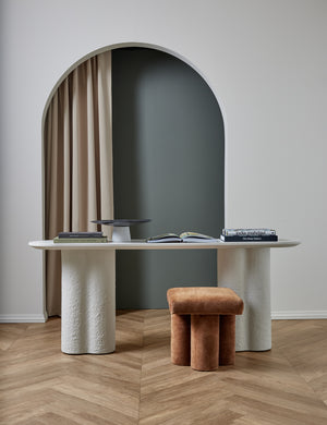The Tatia White Console Table sits in a studio with a cognac velvet ottoman and a centerpiece bowl and books atop it