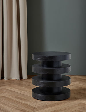 The Pentwater Four-Tiered Black Round Side Table sits in a gray studio room atop chevron hardwood floors