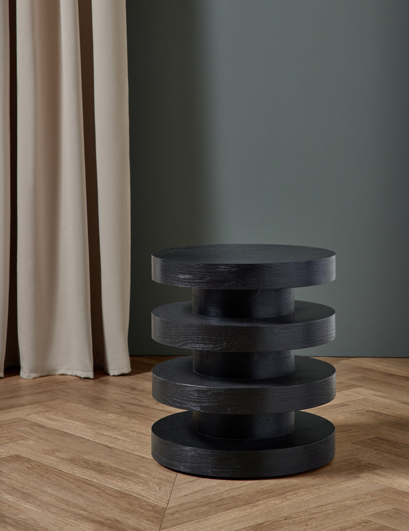 #color::black | The Pentwater Four-Tiered Black Round Side Table sits in a gray studio room atop chevron hardwood floors