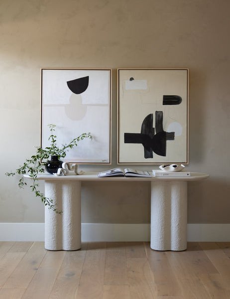 | The In Pursuit Print hangs next to a white wall art above a white sideboard with a black vase and stack of books
