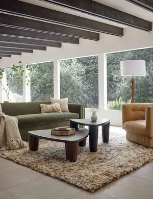 The tegan moroccan shag rug lays in a living room with wooden beamed ceilings under a green velvet sofa and nested coffee tables