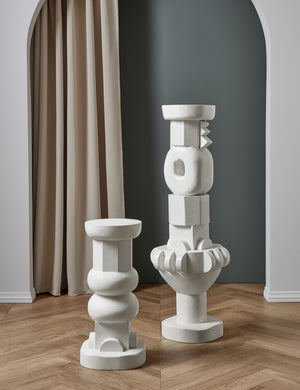 The Toivo short and tall pedestals stand next to each other in a room with a curtain backdrop and chevron floors