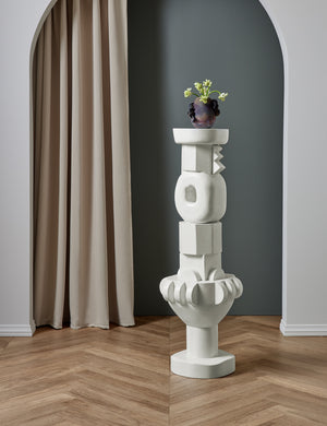 The Toivo tall pedestal stands in a room with a sculptural vase sitting atop it