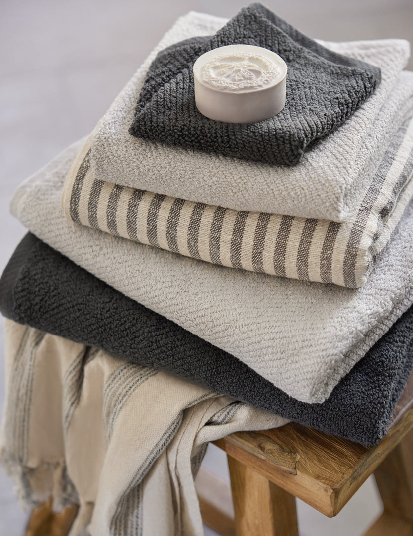 #color::shadow | The midnight gray turkish cotton Air Weight Towel Set by Coyuchi sits in a stack amongst other bathroom towels atop a wooden stool