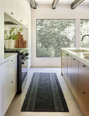 The Adentro geometric flatweave dark blue rug with ivory accents in its runner size lays in a kitchen with white counter tops