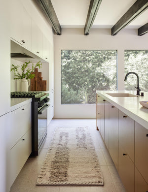 The esha runner rug lays in a kitchen with black hardware, white cabinetry and countertops, and a wooden beamed ceiling
