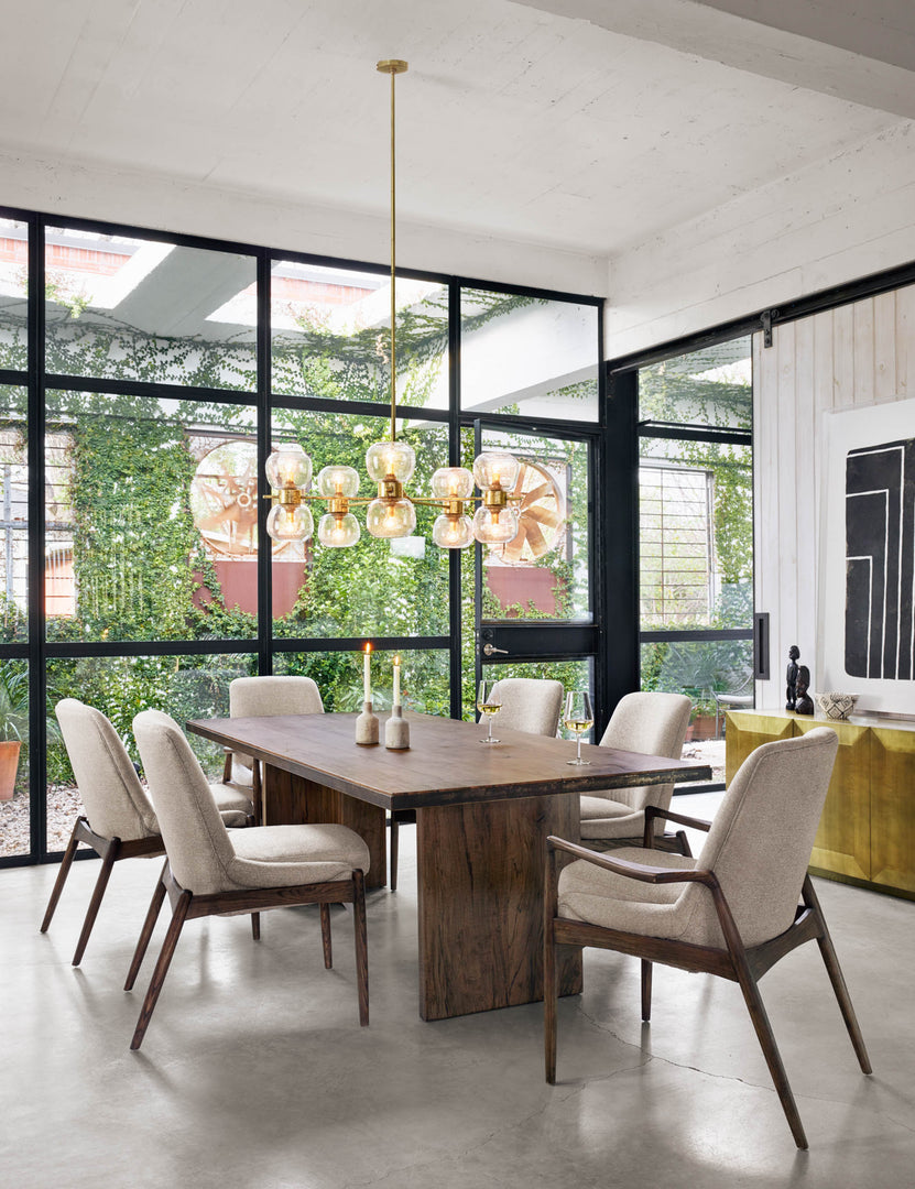 | The Ashbie Dining Table sits in a bright dining room surrounded by six ivory dining chairs under a globe chandelier 