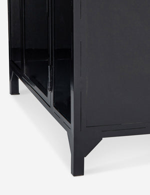Close-up of the bottom right corner of the Cressida matte black iron curio cabinet with glass paneled doors and brass hardware
