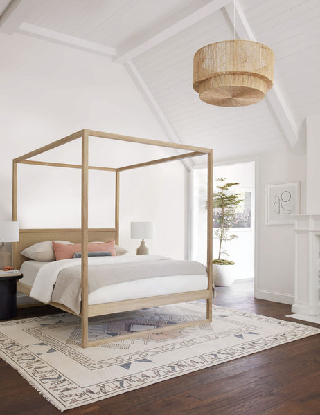 #color::natural | The Sayan natural jute-wrapped pendant light sits in a bedroom with a sloped ceiling, a natural wood canopy bed, and a multicolored geometric rug.