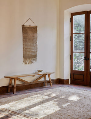 The Nyana natural wall hanging hangs in an entryway above a wooden bench and a plush ivory rug