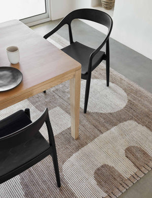 The Abode geometric two-toned kand-knotted floor rug by Élan Byrd with woven border sits in a dining room with black ida dining chairs and a neutral wooden dining table